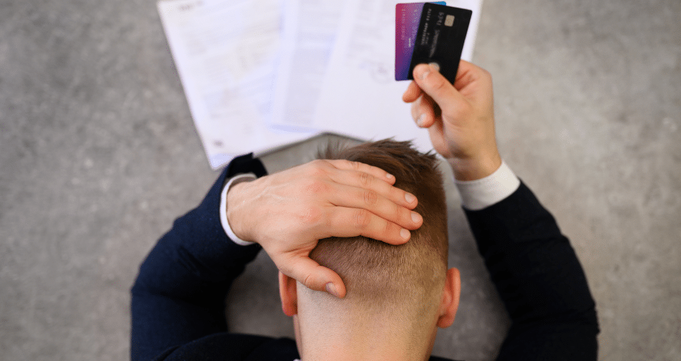 mężczyzna trzymający się za głowę, w prawej dłoni trzyma karty kredytowe